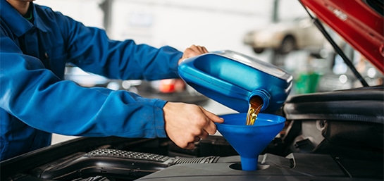 Mecánico de azul cambiando el aceite del motor de un auto rojo.